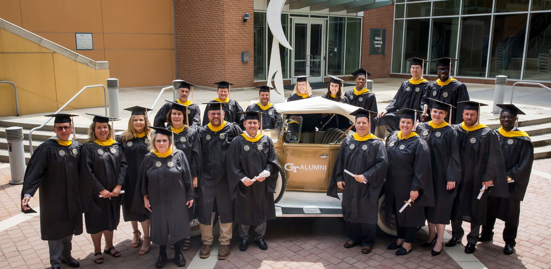Professional Master's in Occupational Safety and Health graduates stand in front of the Ramblin' Wreck in their caps and gowns.