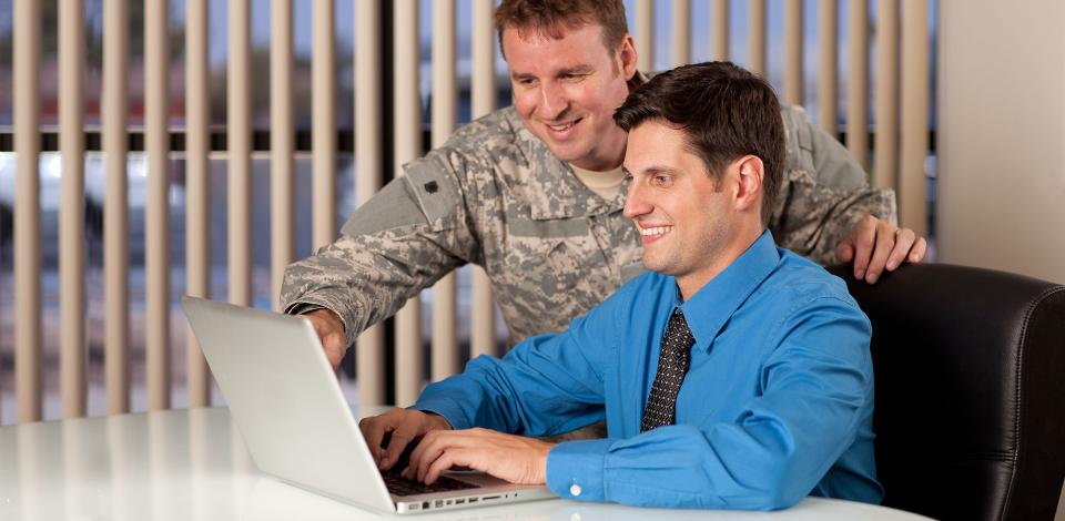 Military personel assisting working professional at computer